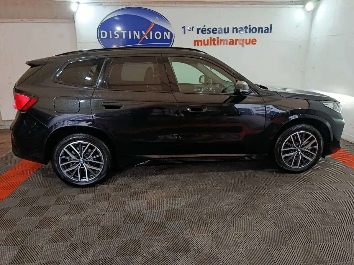BMW X1 xDrive23i M Sport noir vue de profil côté gauche dans un showroom avec jantes alliage distinctives.