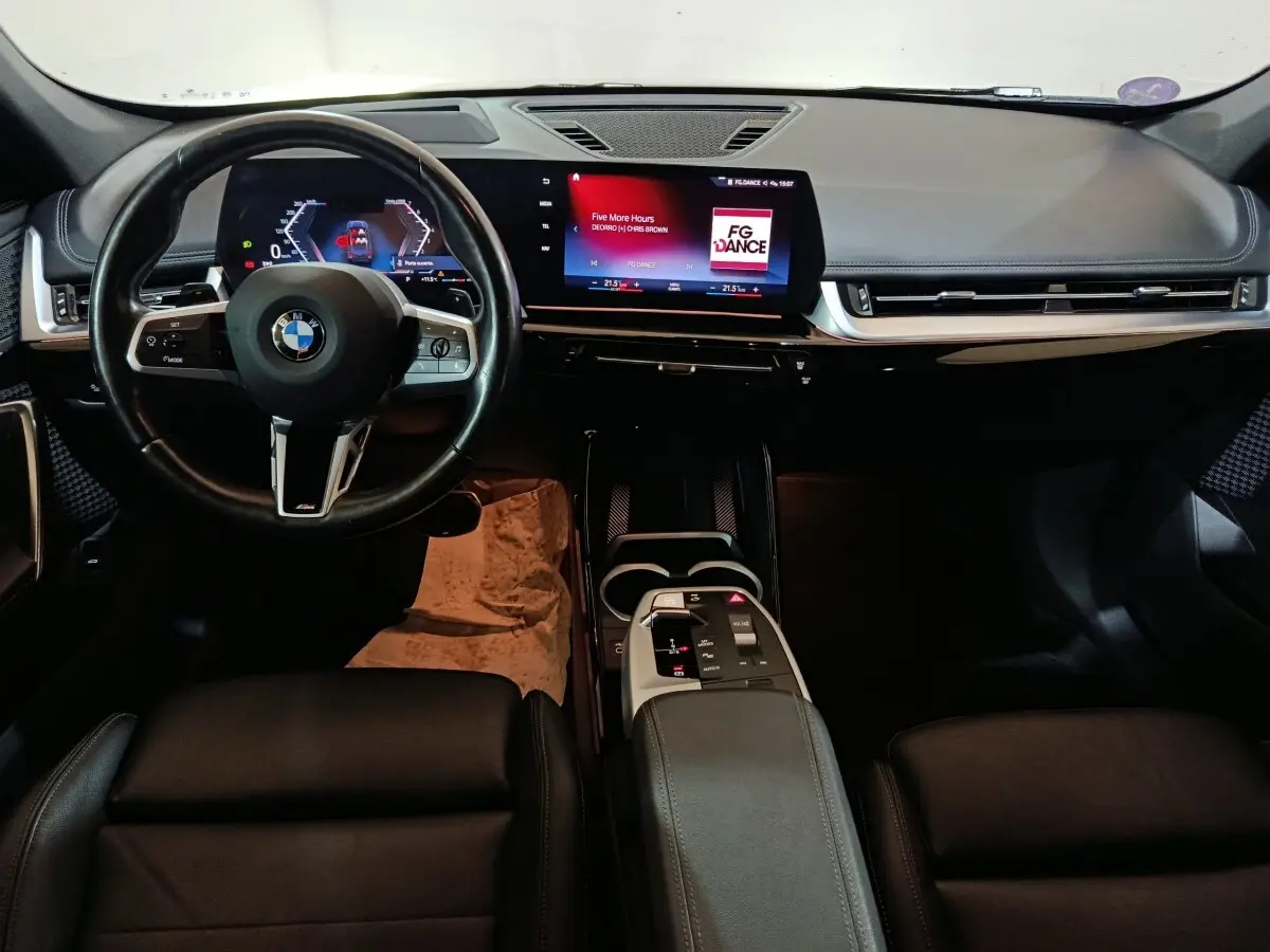 Vue intérieure avant du tableau de bord noir du BMW X1 xDrive23i M Sport avec écran tactile et volant cuir multifonctions.