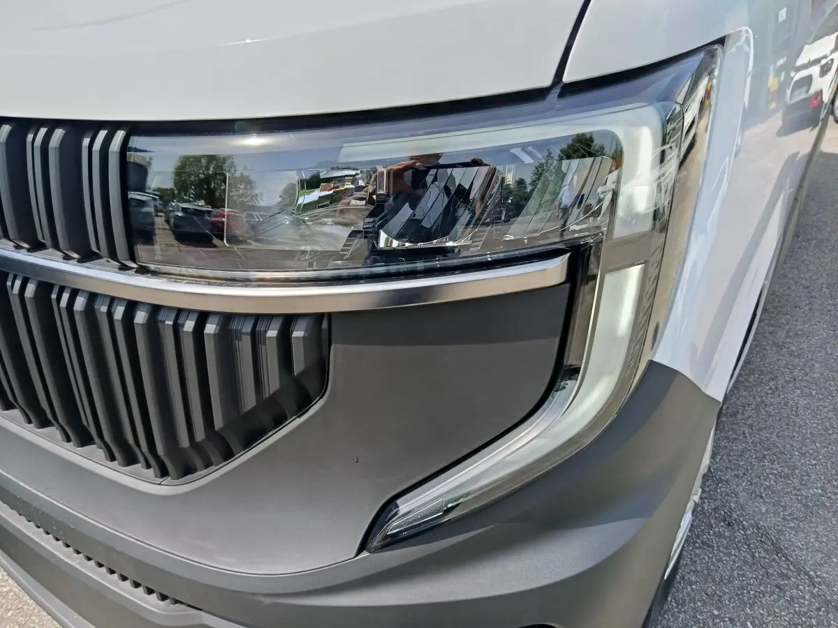 Gros plan sur le phare avant droit et la calandre noire du Renault Master blanc, avec détails modernes et finition mate.