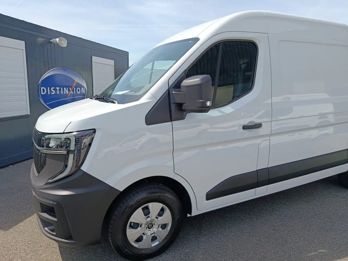 Vue 3/4 avant droit d’un Renault Master blanc avec pare-chocs noirs et rétroviseur noir, stationné devant un bâtiment.