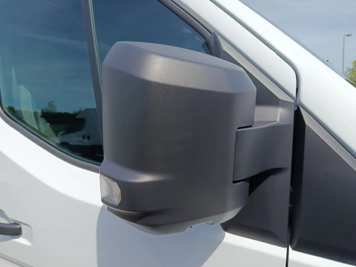 Gros plan sur le rétroviseur droit noir d’un Renault Master blanc, avec fenêtre avant et reflet visible.