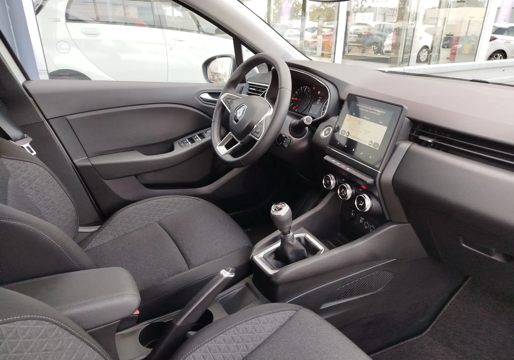 Vue intérieure côté conducteur de la Renault Clio V Business avec tableau de bord moderne et levier de vitesses manuel.