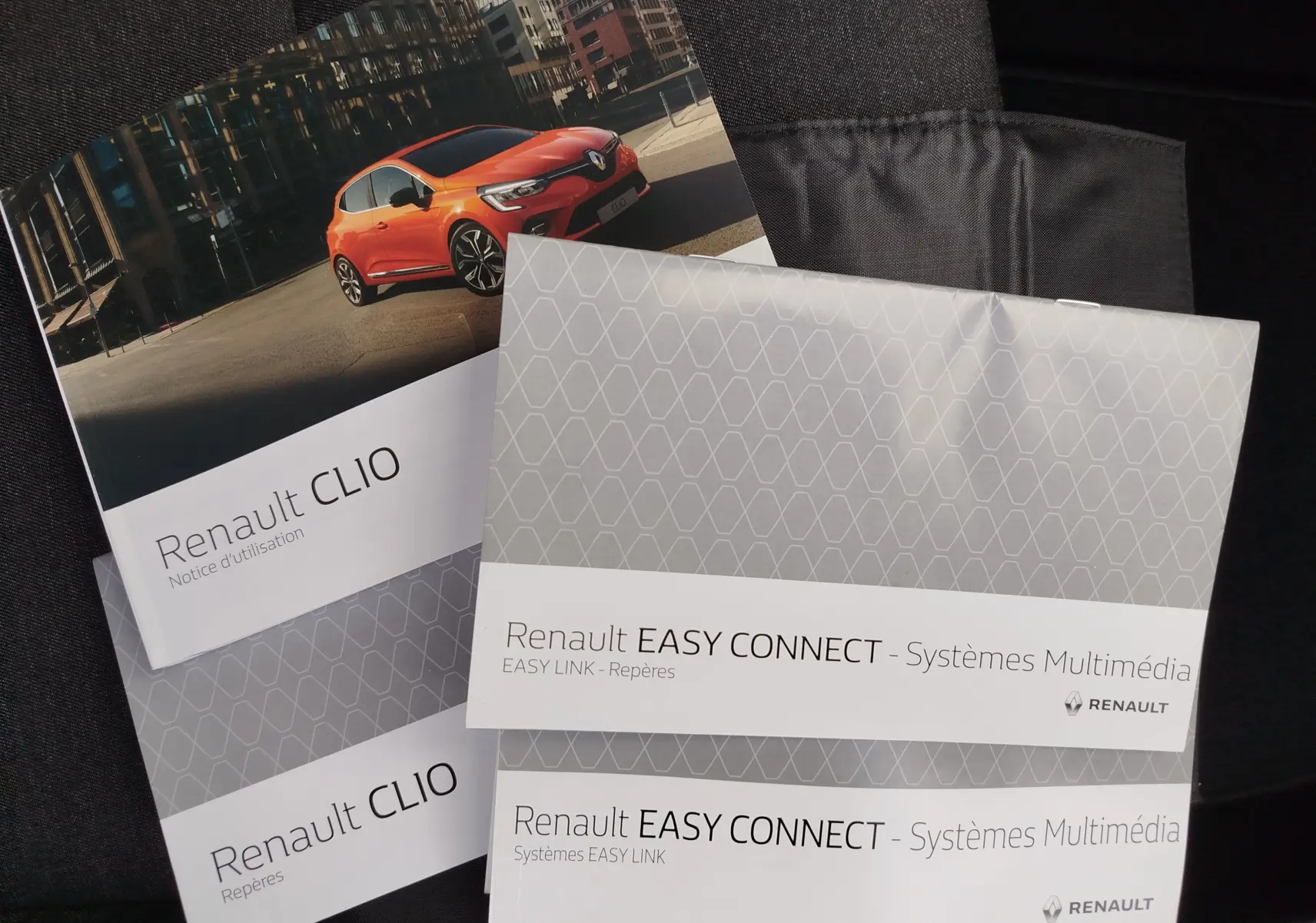 Brochures Renault Clio V avec une photo 3/4 avant d'une Clio orange vif en milieu urbain, sur fond noir.