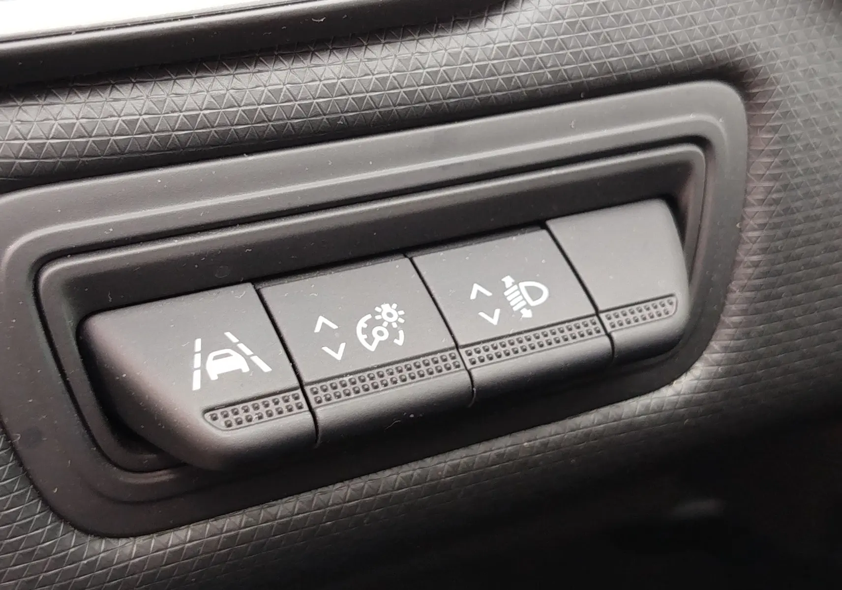 Gros plan sur les boutons de réglage d'assistance à la conduite et d'éclairage dans l'habitacle gris d'une Renault Clio V Business.