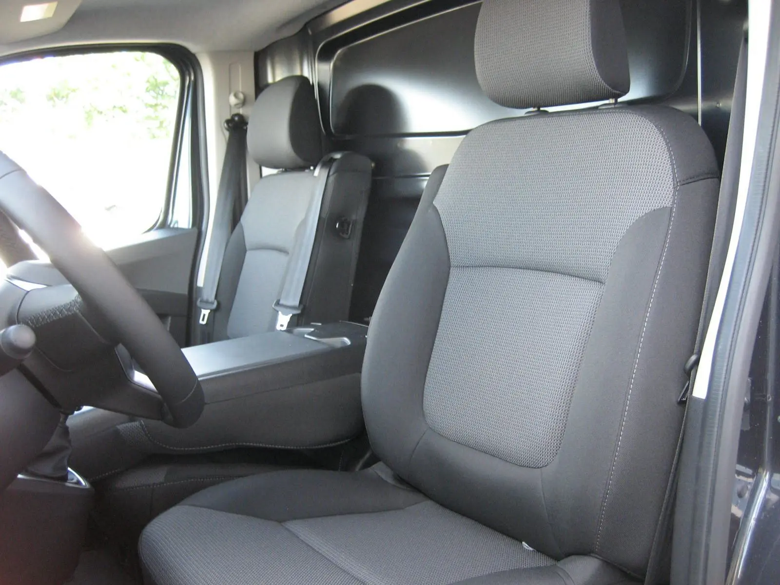 Vue intérieure du Renault Trafic Fourgon gris comète, montrant les sièges avant en tissu gris et le volant côté gauche.