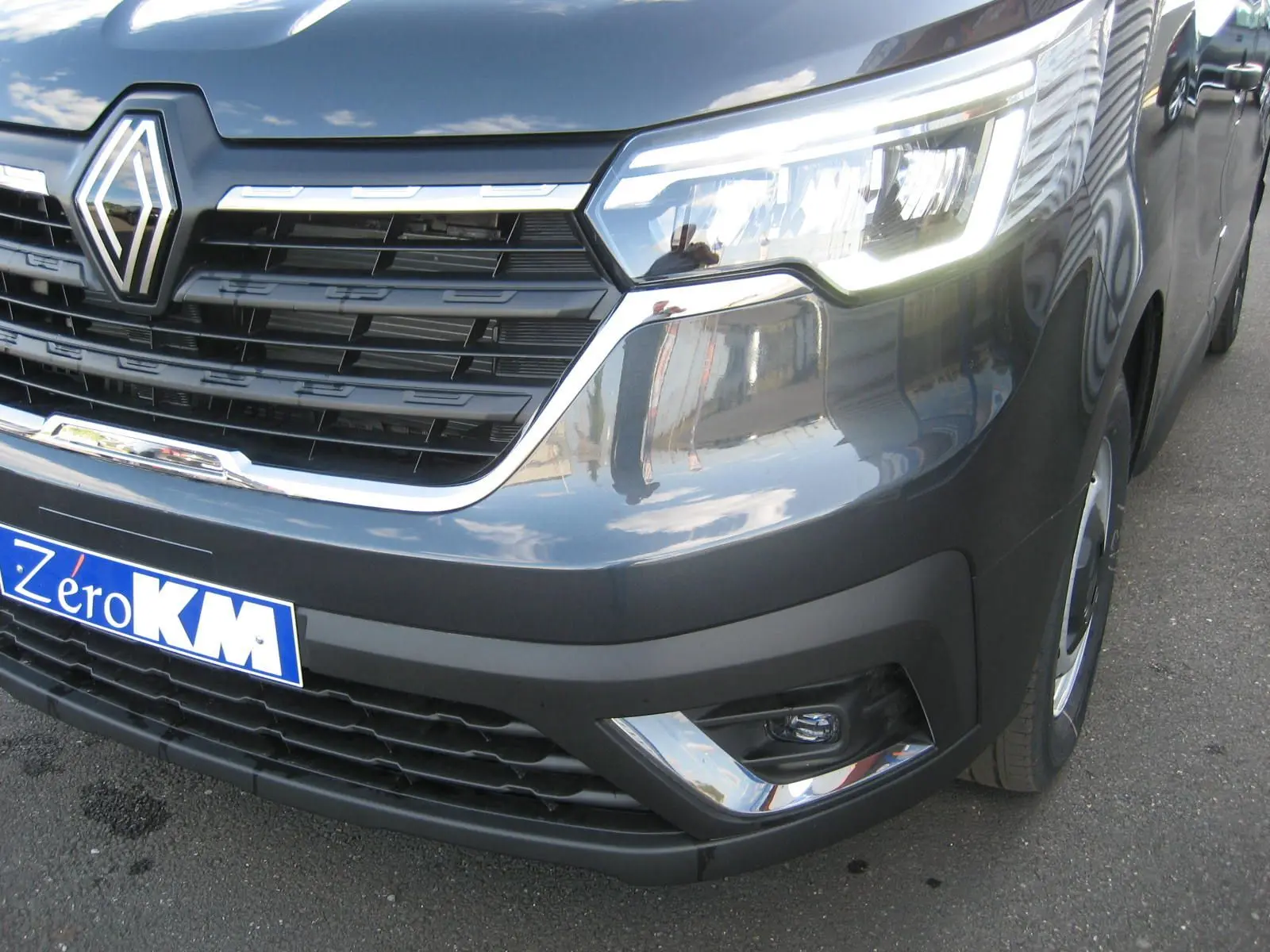 Gros plan sur l'avant droit du Renault Trafic Fourgon gris comète, mettant en valeur la calandre et les phares LED allumés.