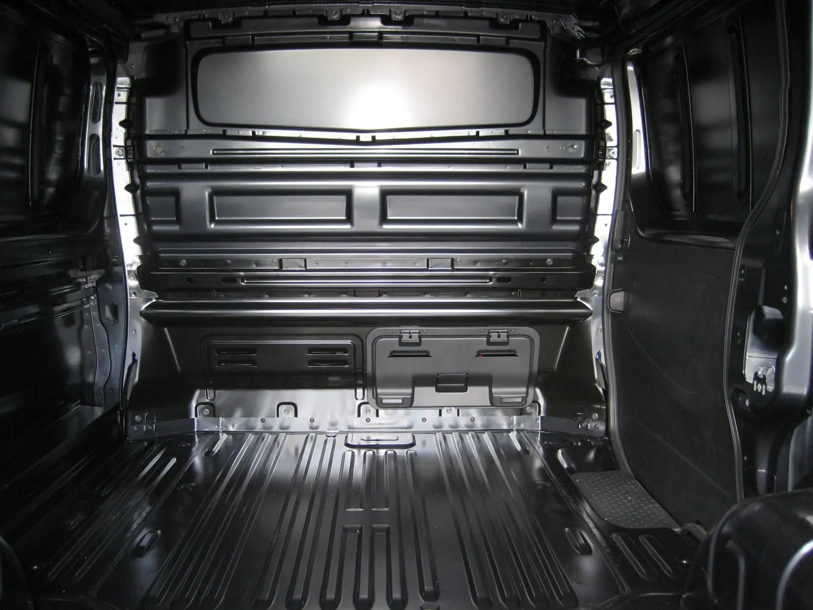 Vue intérieure arrière du fourgon Renault Trafic L1H1 Advance gris comète, montrant l'espace de chargement vide et métallique.