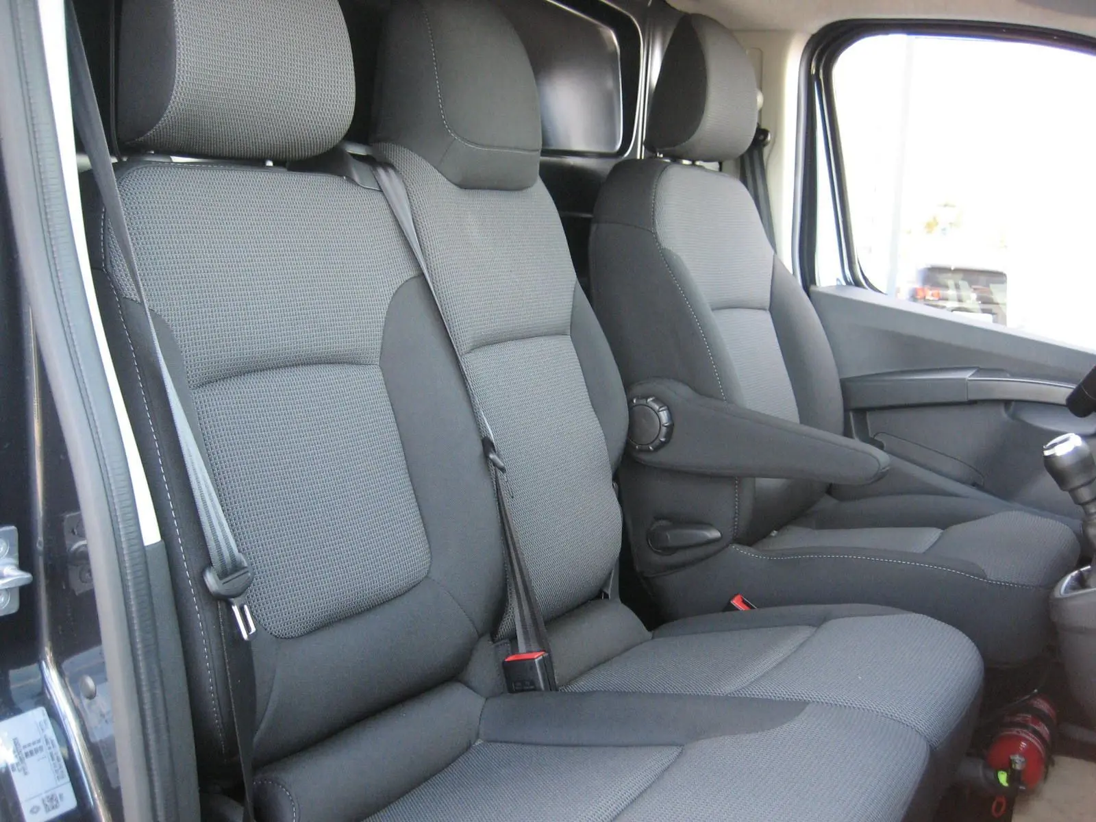 Intérieur du Renault Trafic Fourgon gris comète, vue latérale des sièges avant en tissu gris avec accoudoir côté droit.