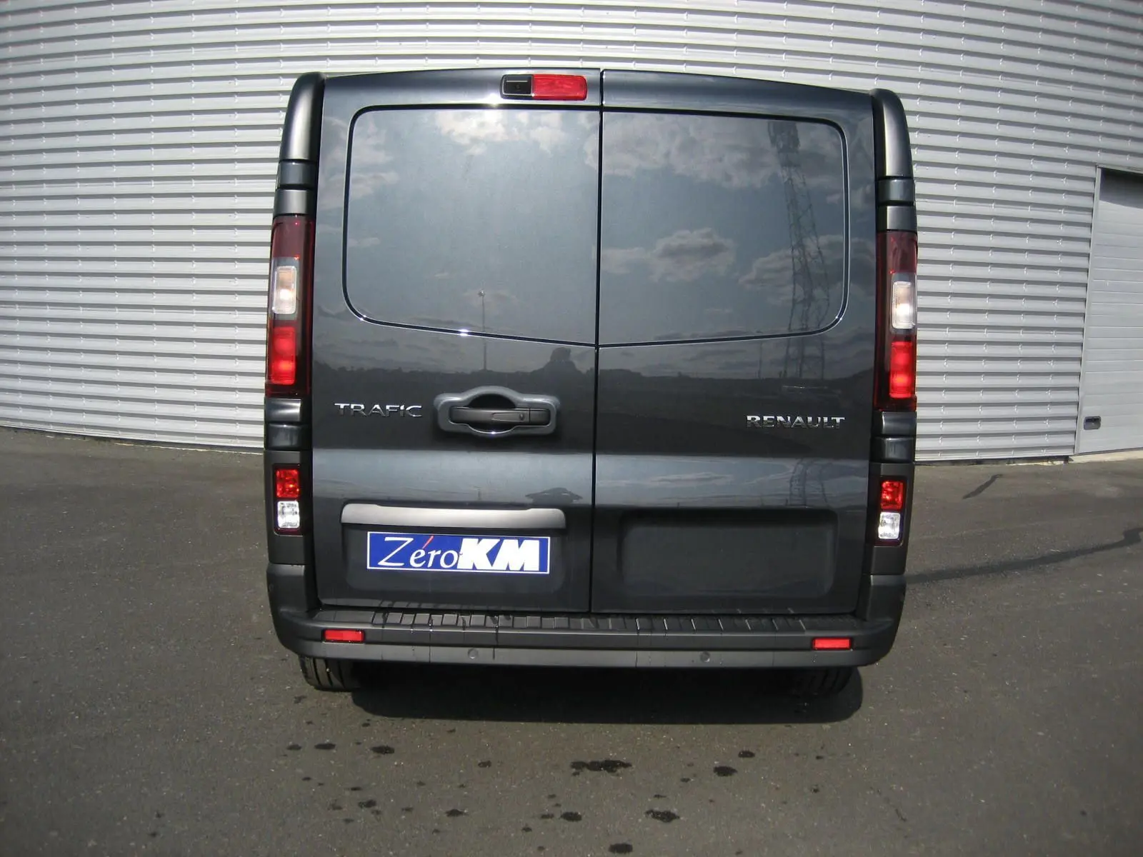 Vue arrière d'un Renault Trafic Fourgon gris comète avec portes battantes et plaque d'immatriculation Zero KM visible.
