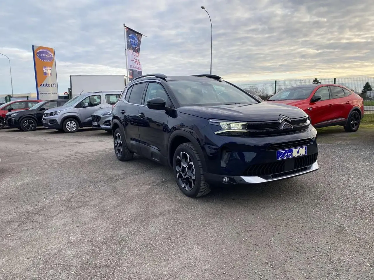 Citroën C5 Aircross bleu Eclipse en 3/4 avant droit sur parking avec autres véhicules en arrière-plan.
