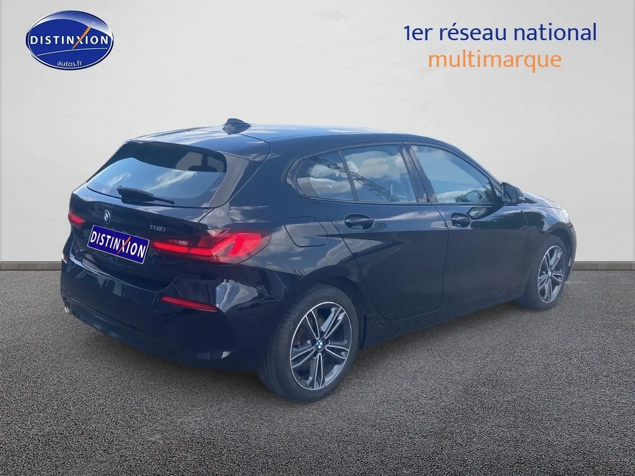 BMW Série 1 noire vue en 3/4 arrière droit, avec jantes alliage et feux arrière LED allumés.