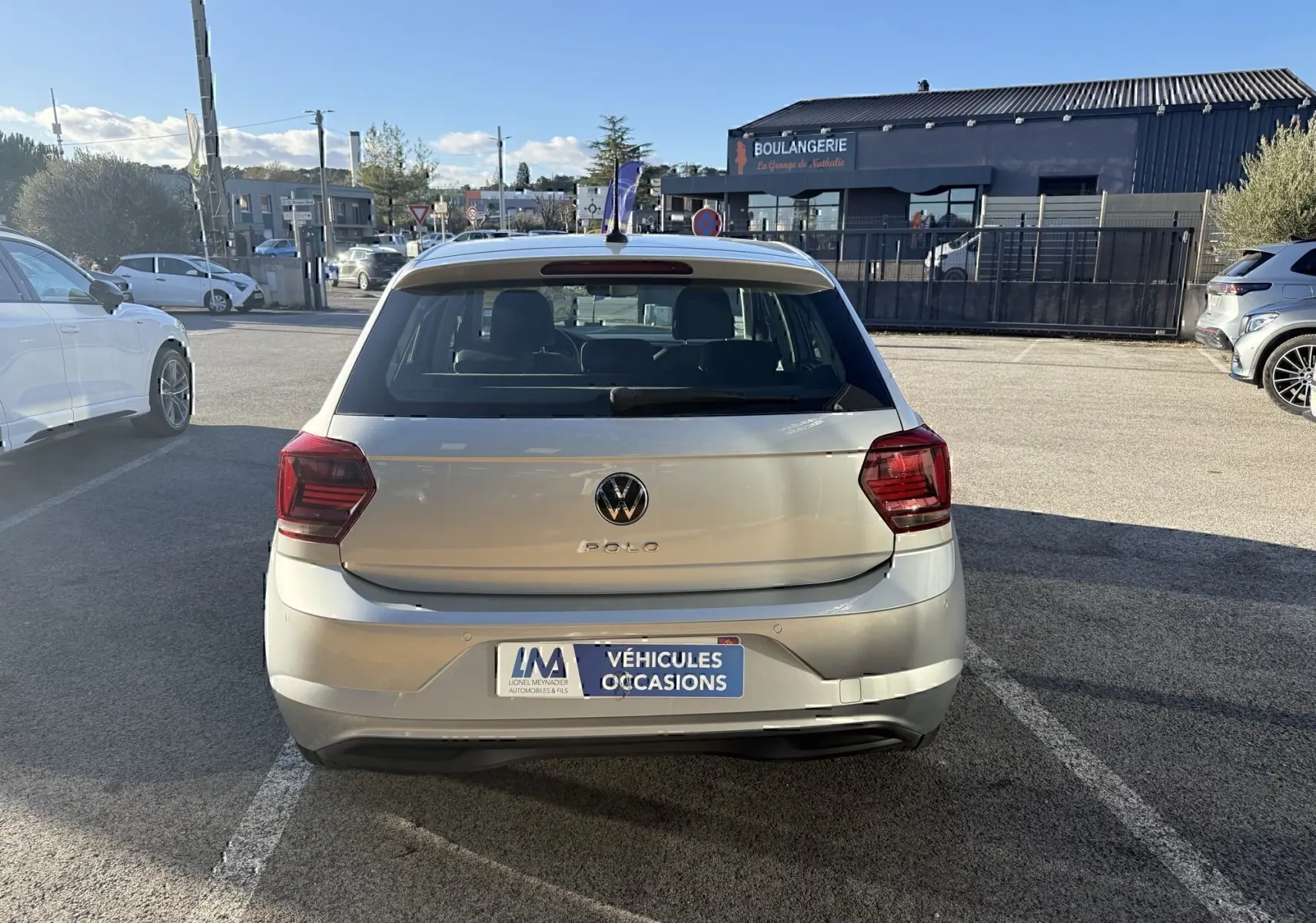 Vue arrière d'une Volkswagen Polo gris métal 2021 garée sur un parking en plein jour avec plaque "Véhicules Occasions".