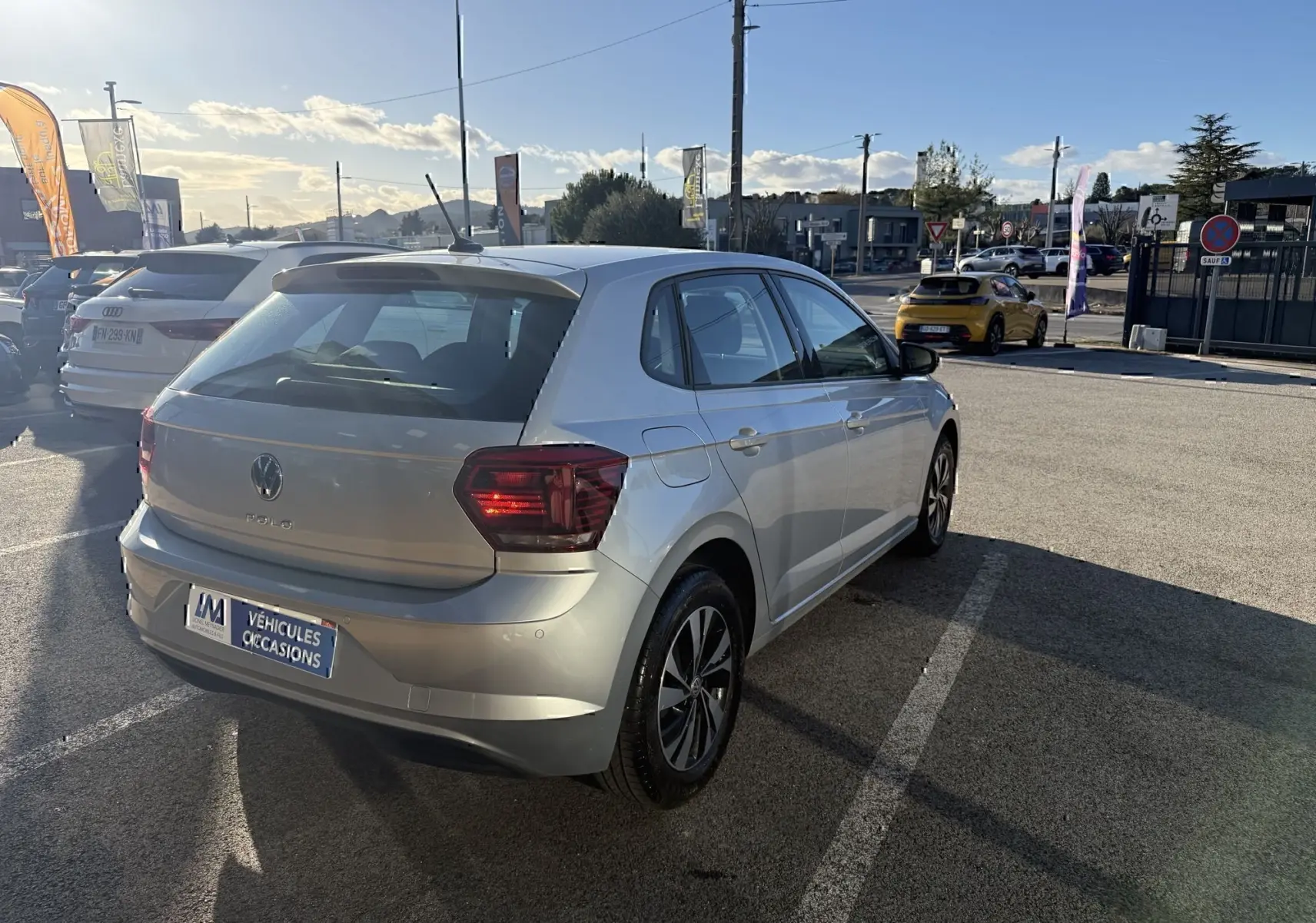 Volkswagen Polo gris métal vue 3/4 arrière droit sur parking, avec feux arrière et jantes distinctives visibles.