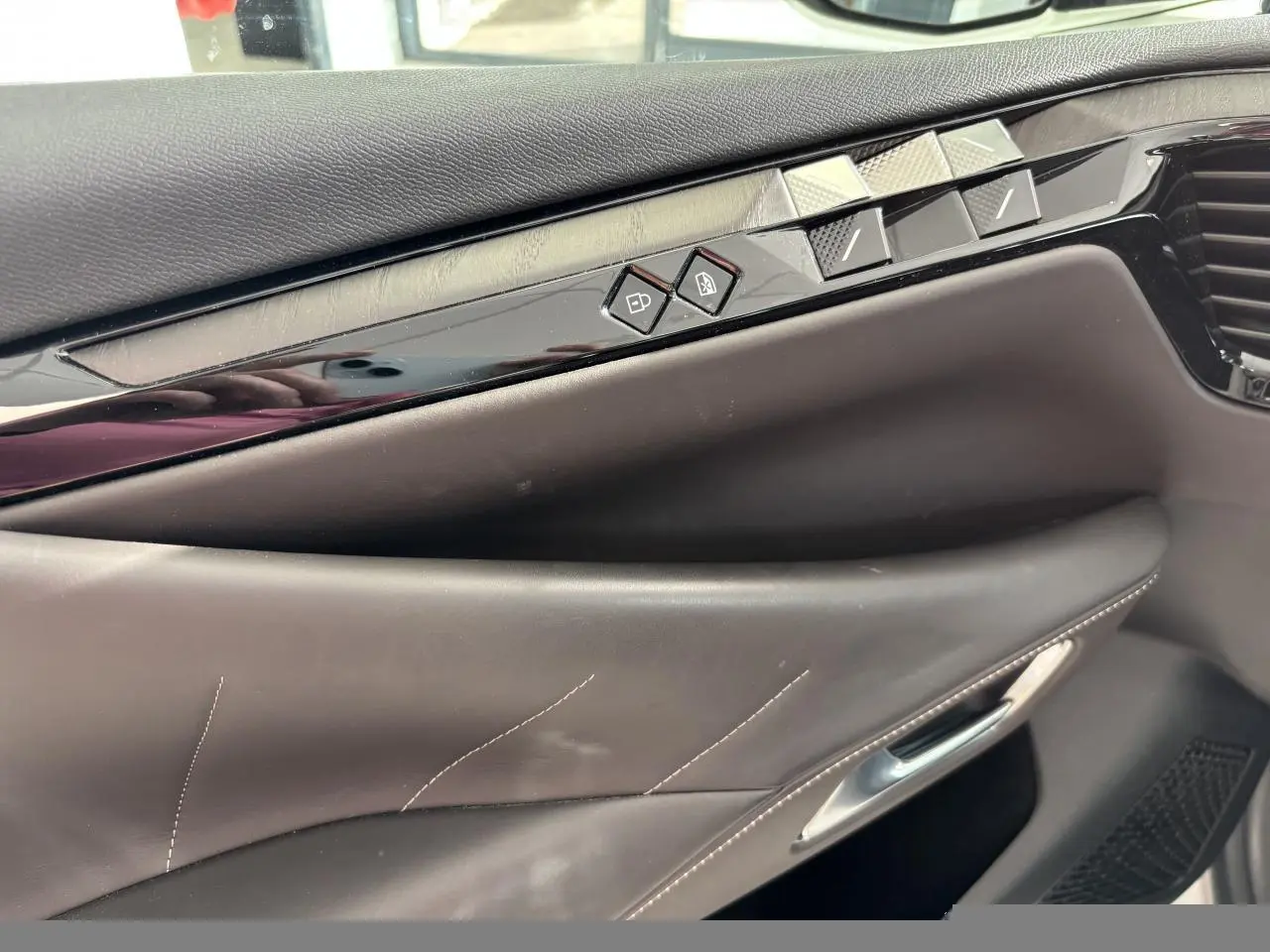 Détail de la porte avant droite du DS4 2023, cuir brun Criollo avec boutons de commande et insert noir brillant.