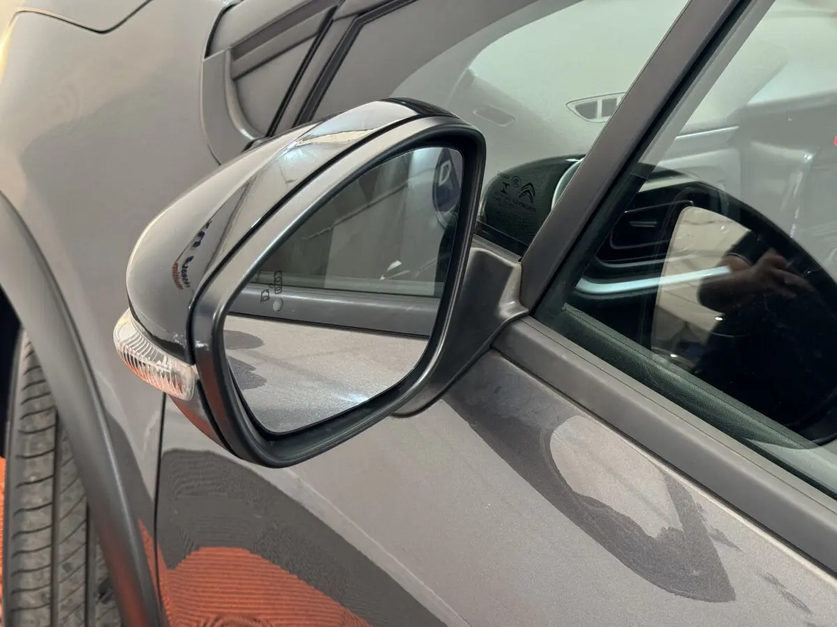 Rétroviseur côté conducteur d'une Citroën C3 gris foncé, avec clignotant intégré, vue rapprochée.