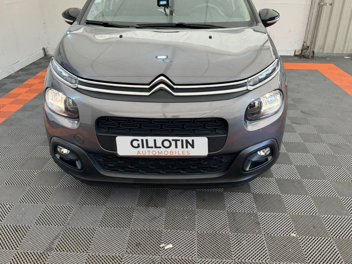 Vue avant d'une Citroën C3 gris foncé avec phares LED et calandre noire distinctive sur sol damier.