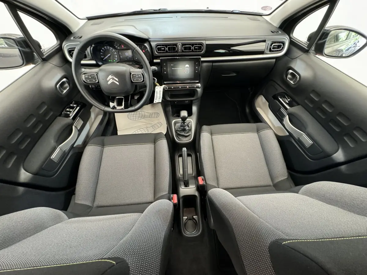 Vue intérieure avant de la Citroën C3 2020, tableau de bord noir brillant avec écran tactile et sièges tissu gris clair.
