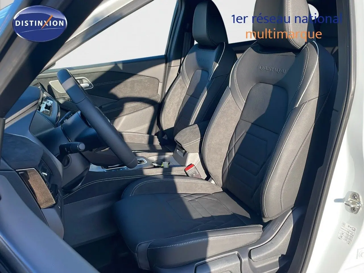 Intérieur du Nissan Qashqai blanc nacré, vue côté conducteur, sièges noirs en cuir avec surpiqûres blanches et logo Qashqai.