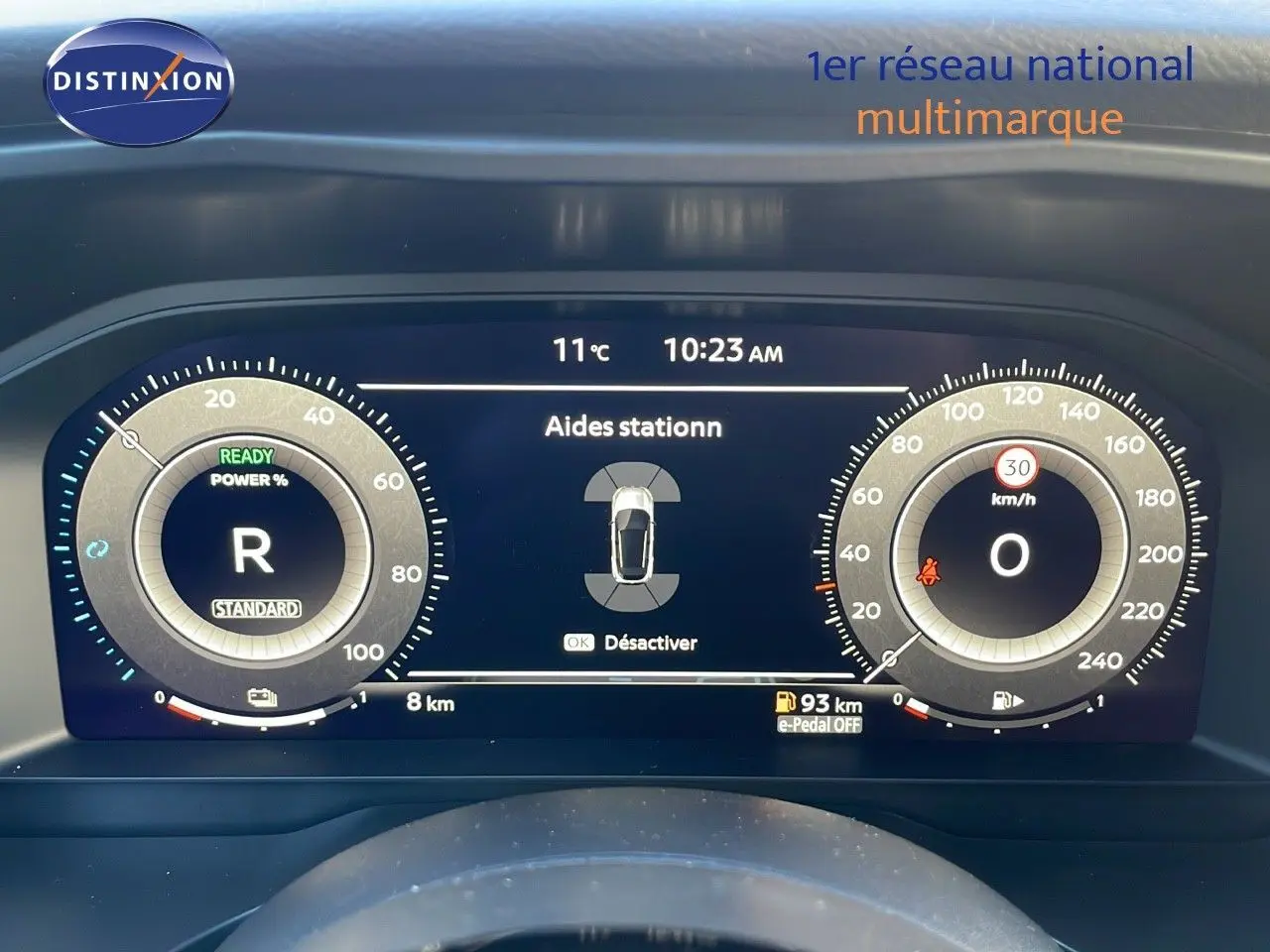 Tableau de bord numérique du Nissan Qashqai blanc nacré, affichant l'aide au stationnement et la vitesse à 0 km/h.