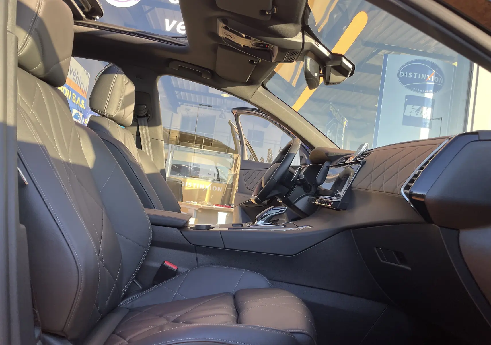 Intérieur noir cuir du DS7 2024 vu côté conducteur, avec tableau de bord moderne et toit panoramique ouvert.