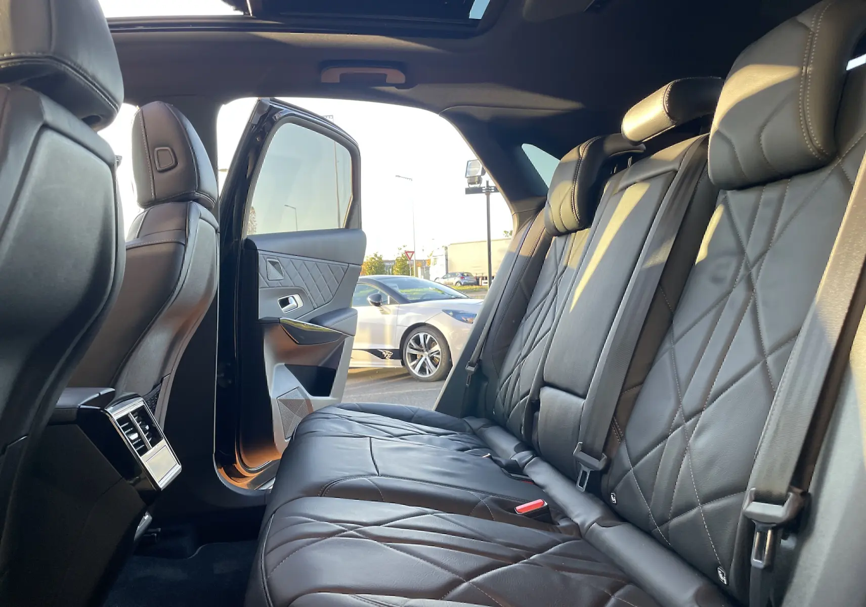 Vue intérieure arrière du DS7 2024 noir Perla Nera, montrant les sièges en cuir noir matelassé et la porte arrière ouverte.