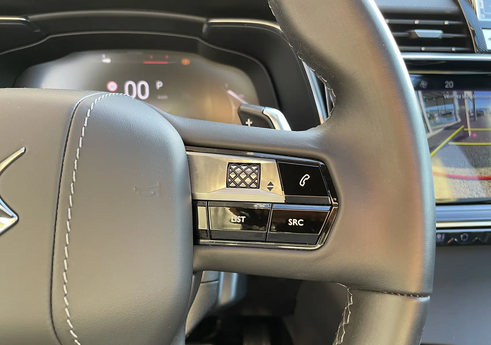 Gros plan sur le côté droit du volant en cuir noir du DS7 2024, avec commandes audio et écran de caméra de recul visible.