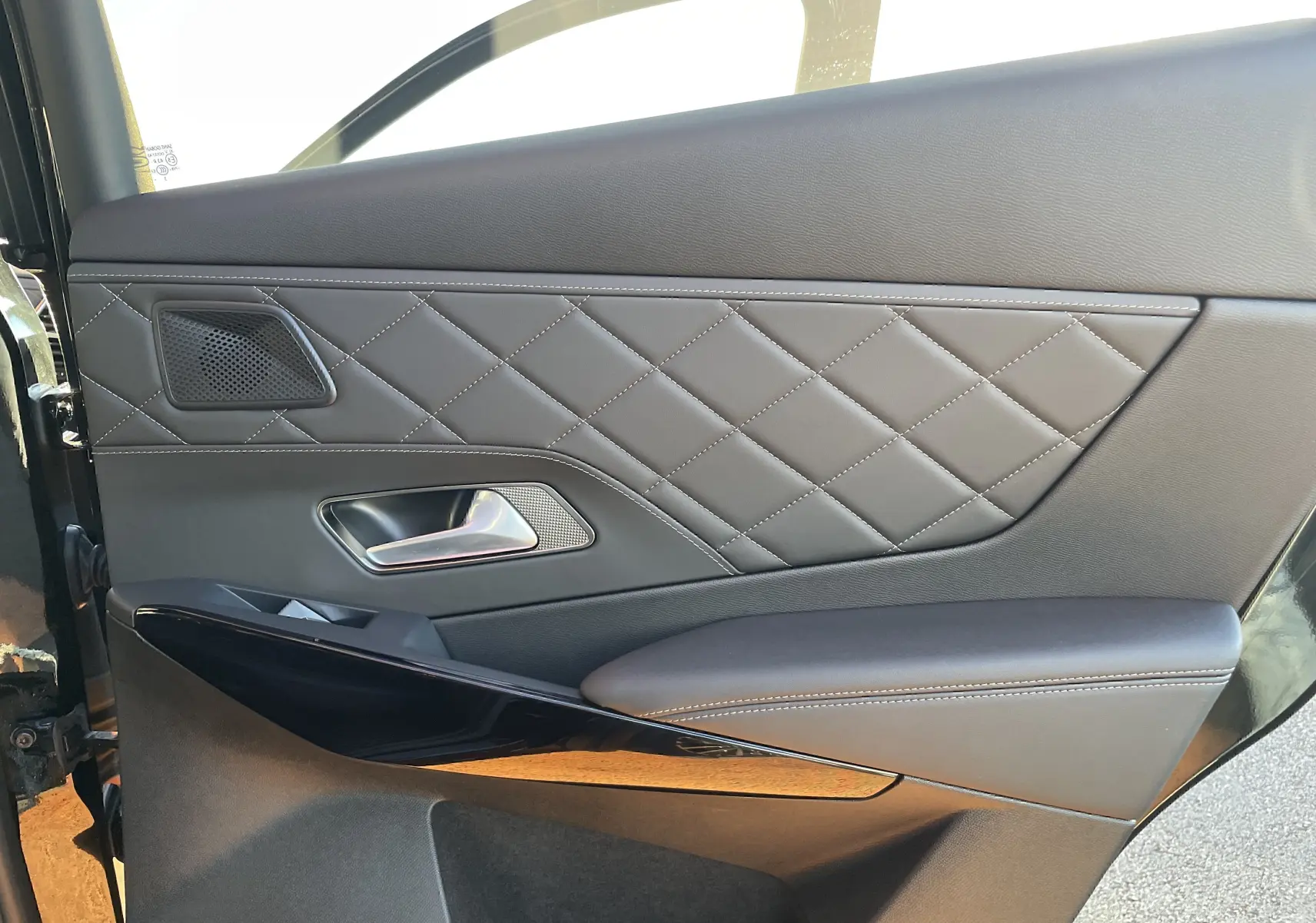 Gros plan sur la porte côté gauche du DS7 2024 noir Perla Nera, avec cuir noir matelassé et surpiqûres blanches.