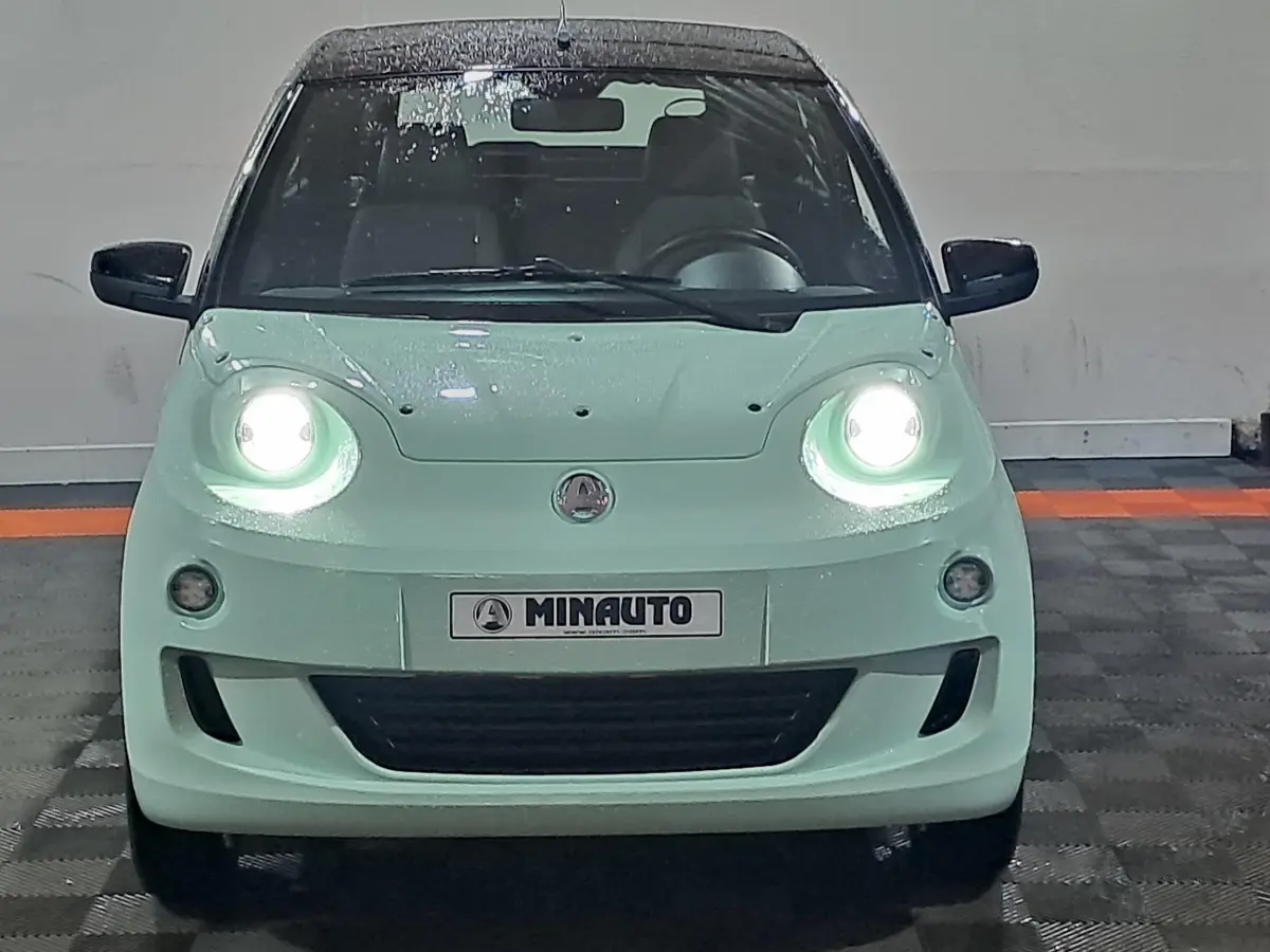 Vue frontale d'une AIXAM MINAUTO E chic 2025 verte avec phares allumés et rétroviseurs caméra côté gauche.