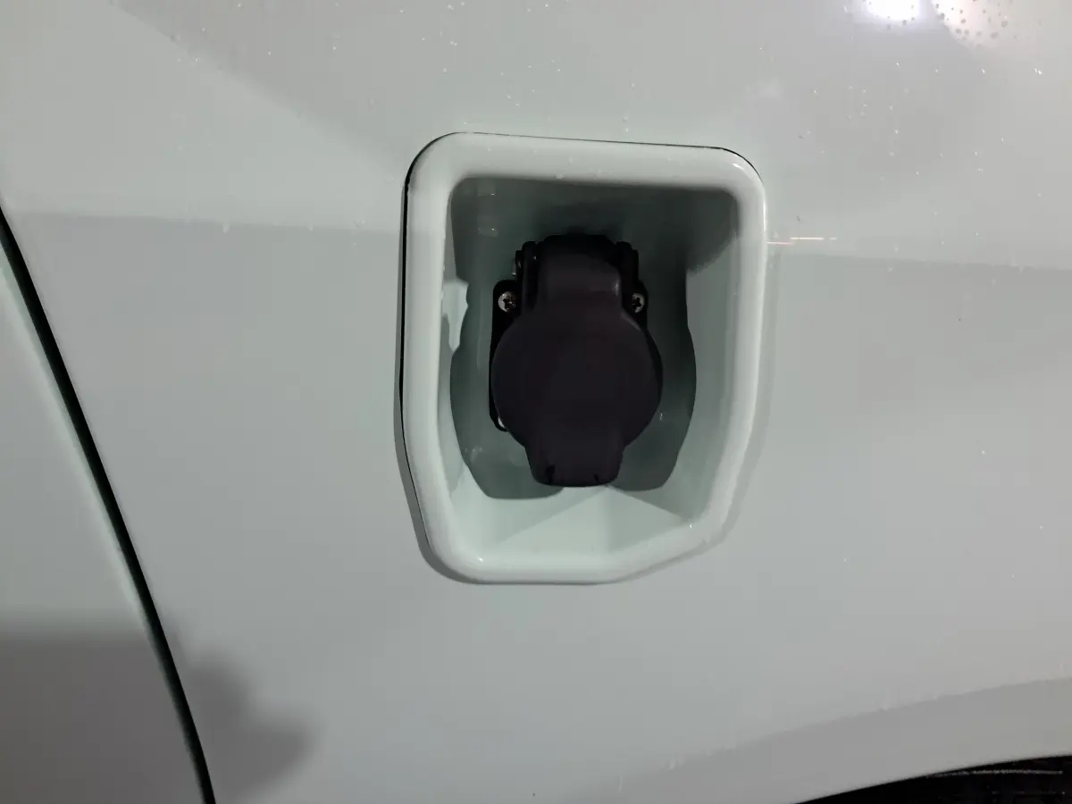 Prise de recharge électrique fermée sur la carrosserie blanche d'une Aixam Minauto E chic 2025, côté conducteur.