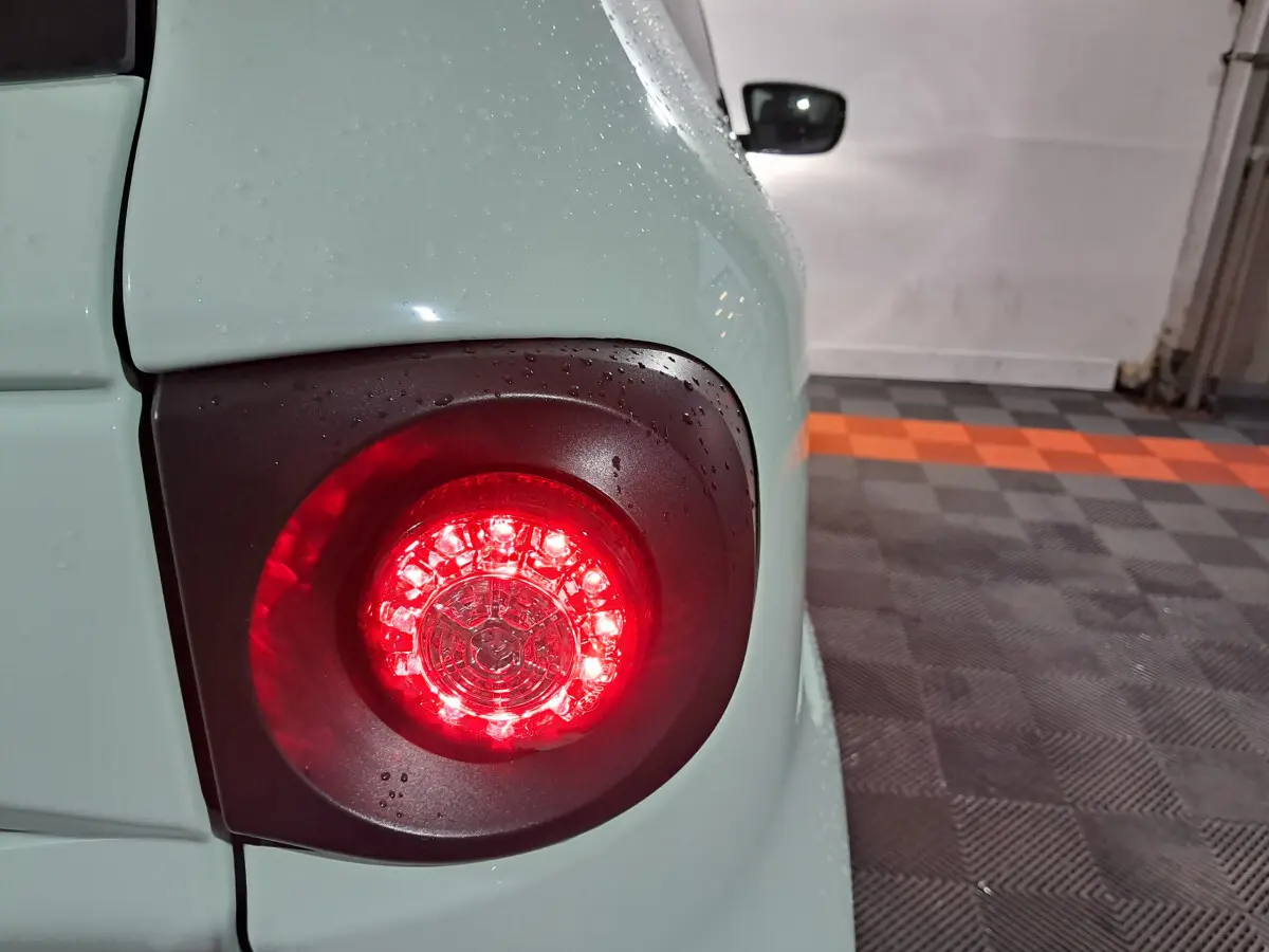 Gros plan sur le feu arrière droit rouge d'une Aixam Minauto E chic 2025 vert électrique avec gouttes d'eau.