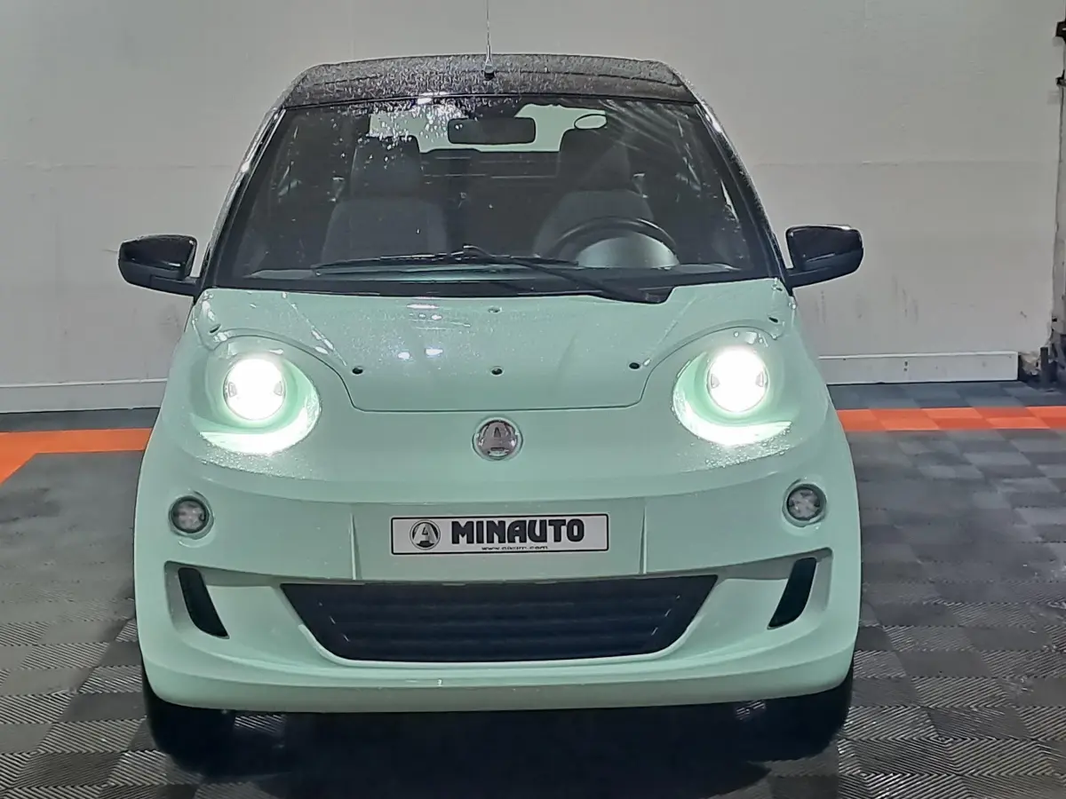 Vue frontale d'une Aixam MINAUTO E chic 2025 verte électrique avec phares allumés et rétroviseurs noirs.