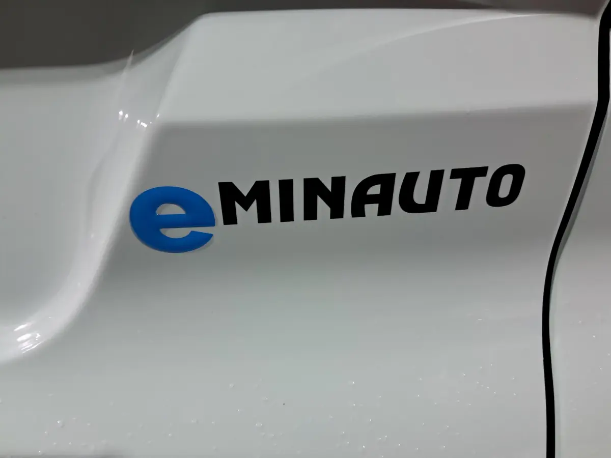 Gros plan sur le logo eMINAUTO en bleu et noir sur la carrosserie verte de l'AIXAM MINAUTO E chic côté conducteur.