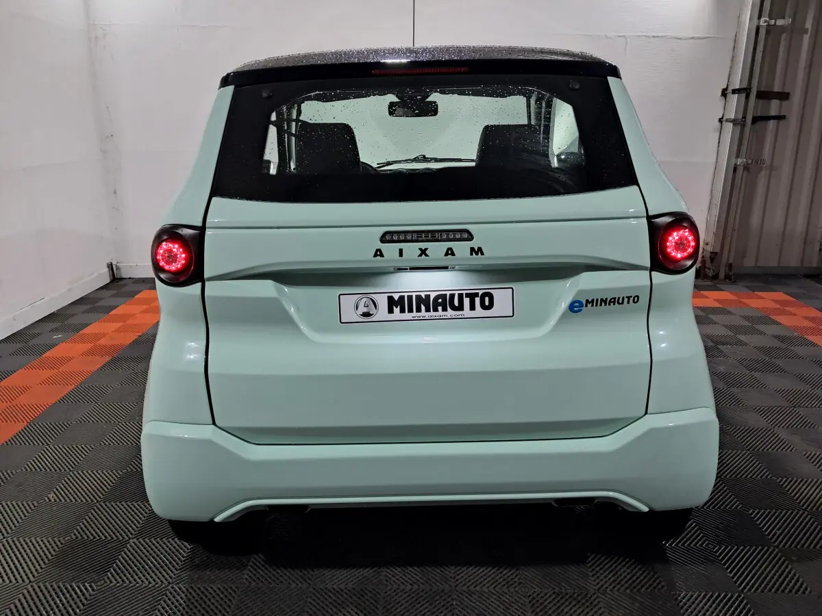 Vue arrière d'une AIXAM MINAUTO E chic 2025 verte avec feux ronds allumés et logo eMINAUTO visible à droite.