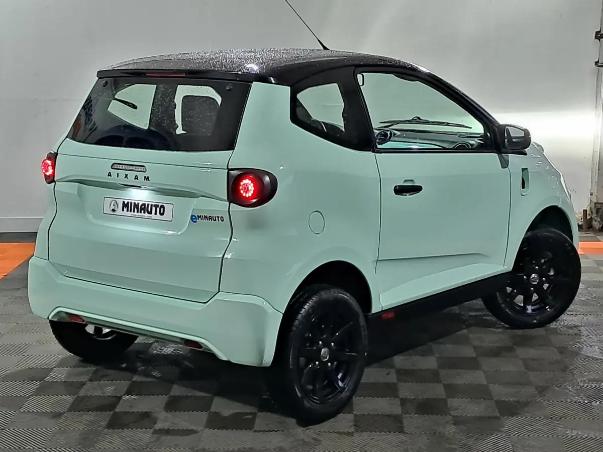 Vue 3/4 arrière droite d'une Aixam MINAUTO E chic électrique vert clair avec jantes noires et caméra sur le côté conducteur.