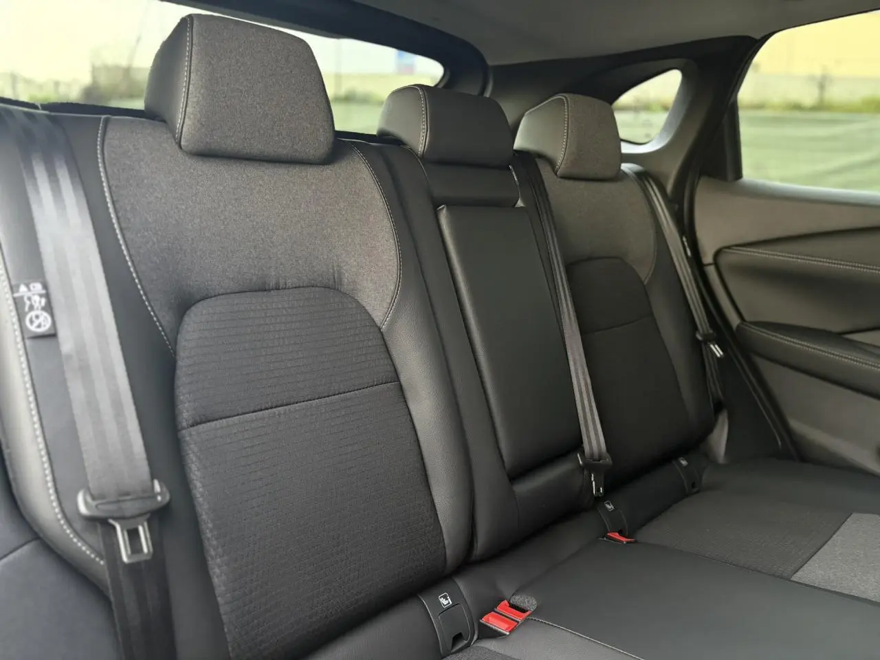 Vue intérieure arrière du Nissan Qashqai 2025, sièges tissu et cuir noirs avec ceinture de sécurité visible.