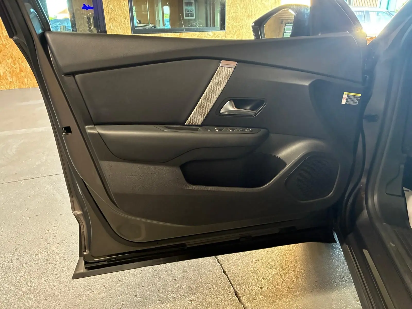 Vue intérieure de la porte avant gauche d'une Citroën C4 X gris 2024, avec garniture noire et commandes électriques.