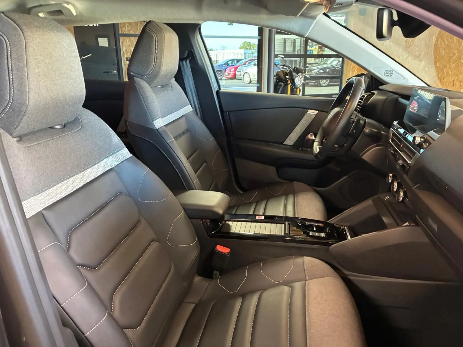 Vue intérieure côté conducteur de la Citroën C4 X 1.5 BlueHDi 130 gris, sièges tissu et cuir bicolore, tableau de bord moderne.