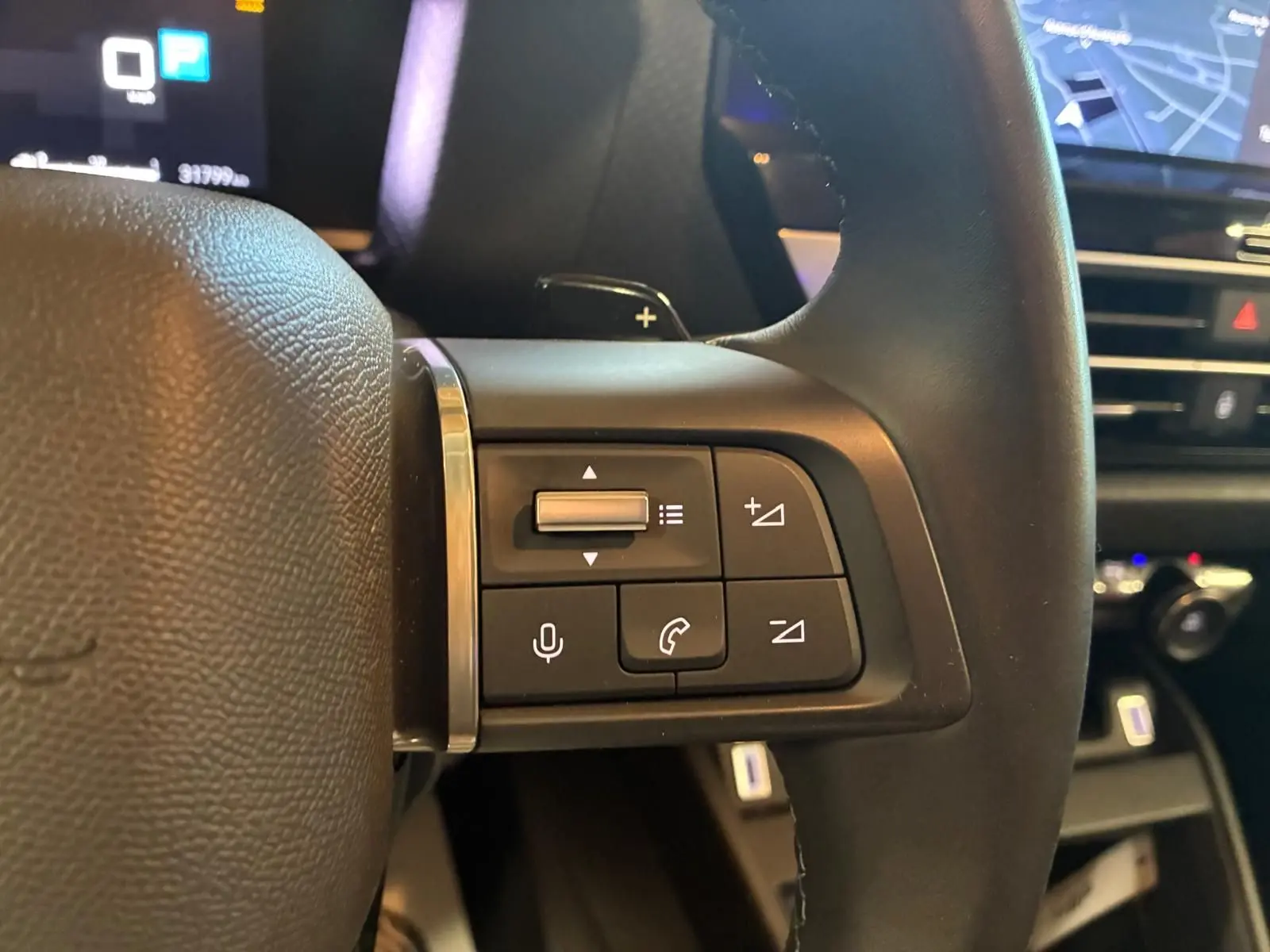 Gros plan sur les commandes au volant côté gauche du Citroën C4 X gris 2024, avec tableau de bord et écran GPS en arrière-plan.