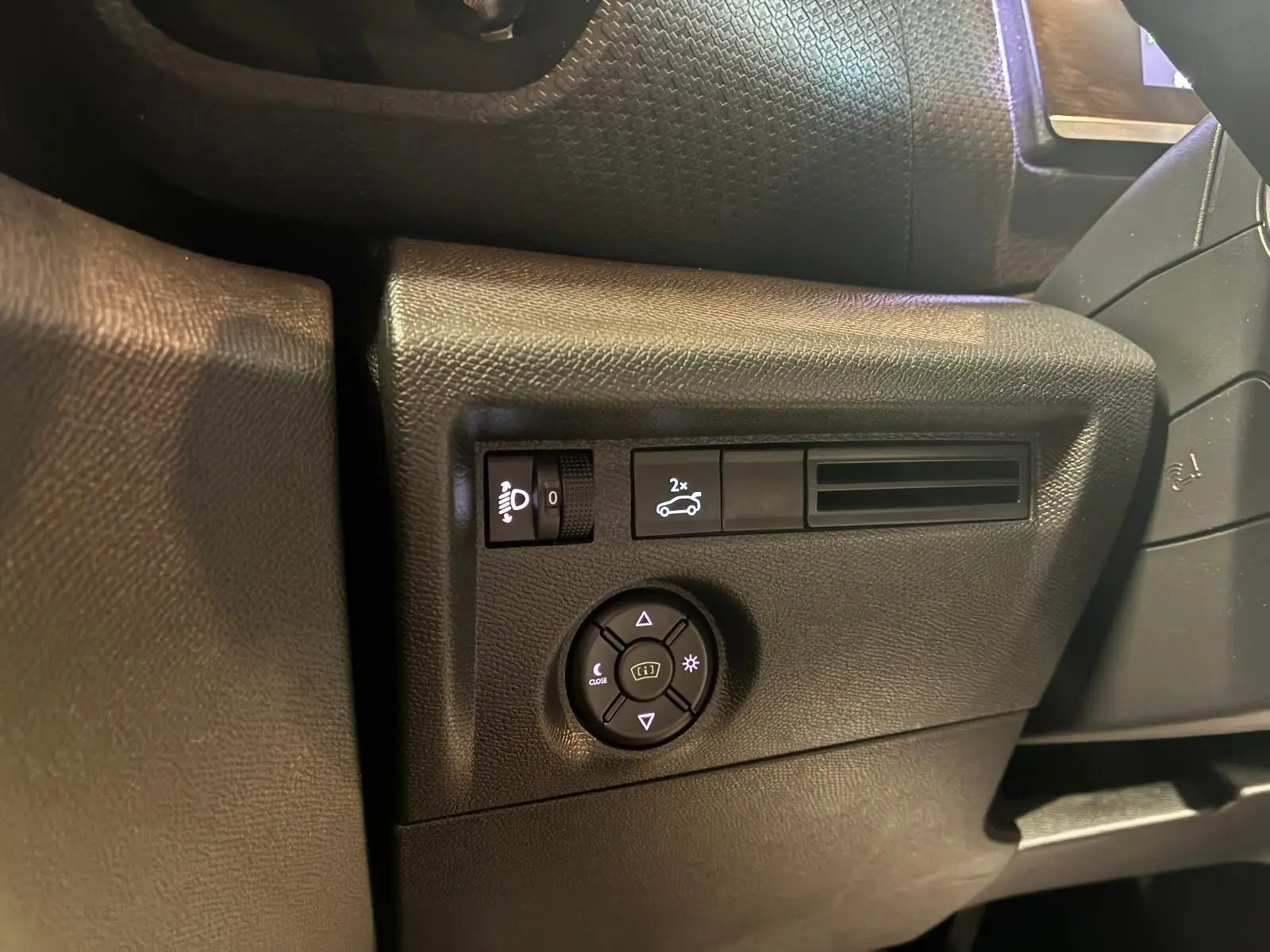 Détail du tableau de bord côté gauche du Citroën C4 X gris 2024, avec commandes d'éclairage et réglage des rétroviseurs.