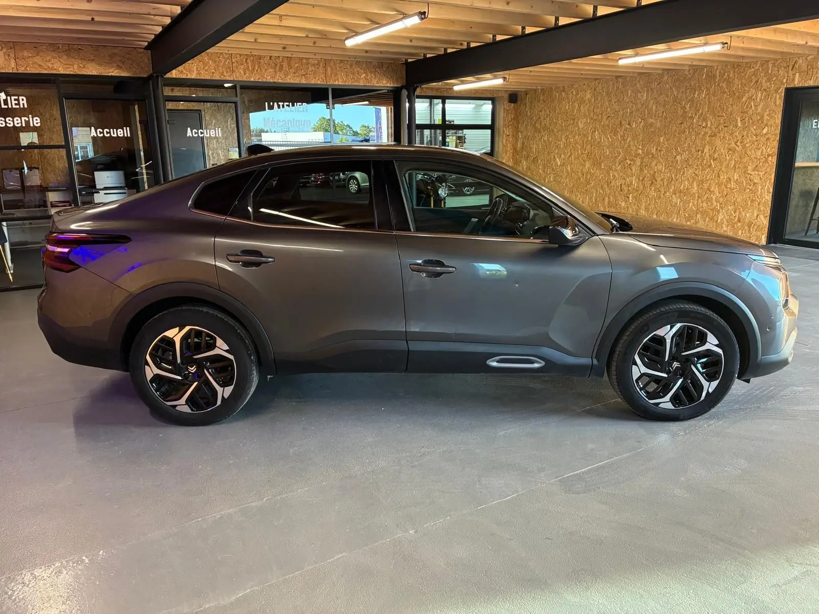 Vue de profil côté gauche d'une Citroën C4 X gris 2024 avec jantes noires et détails de carrosserie noirs.