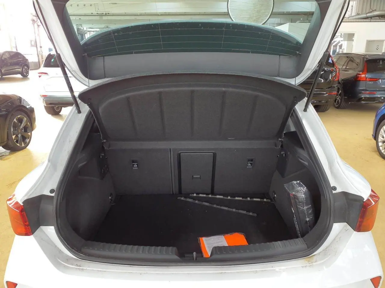 Coffre ouvert vu de l'arrière d'une CUPRA Leon blanc Nevada, montrant l'espace de chargement vide avec quelques objets.