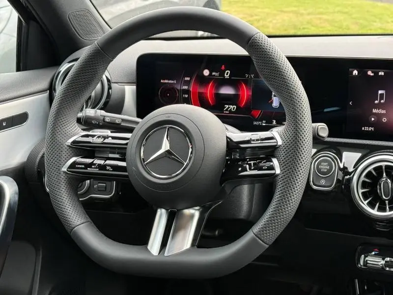 Vue rapprochée du volant sport cuir perforé et des écrans numériques du tableau de bord d'une Mercedes Classe A gris montagne.
