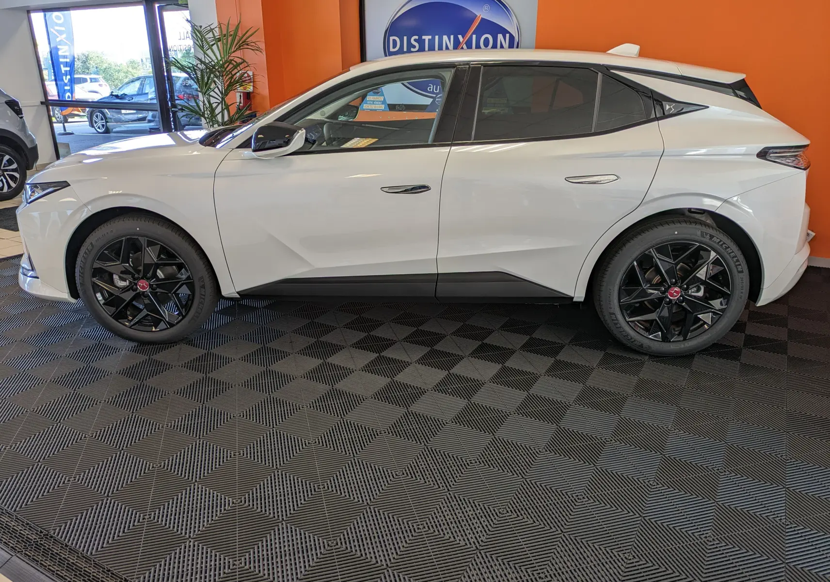 Profil côté gauche d'une DS4 blanche nacrée 2024 avec jantes alliage noires 19 pouces dans un showroom.
