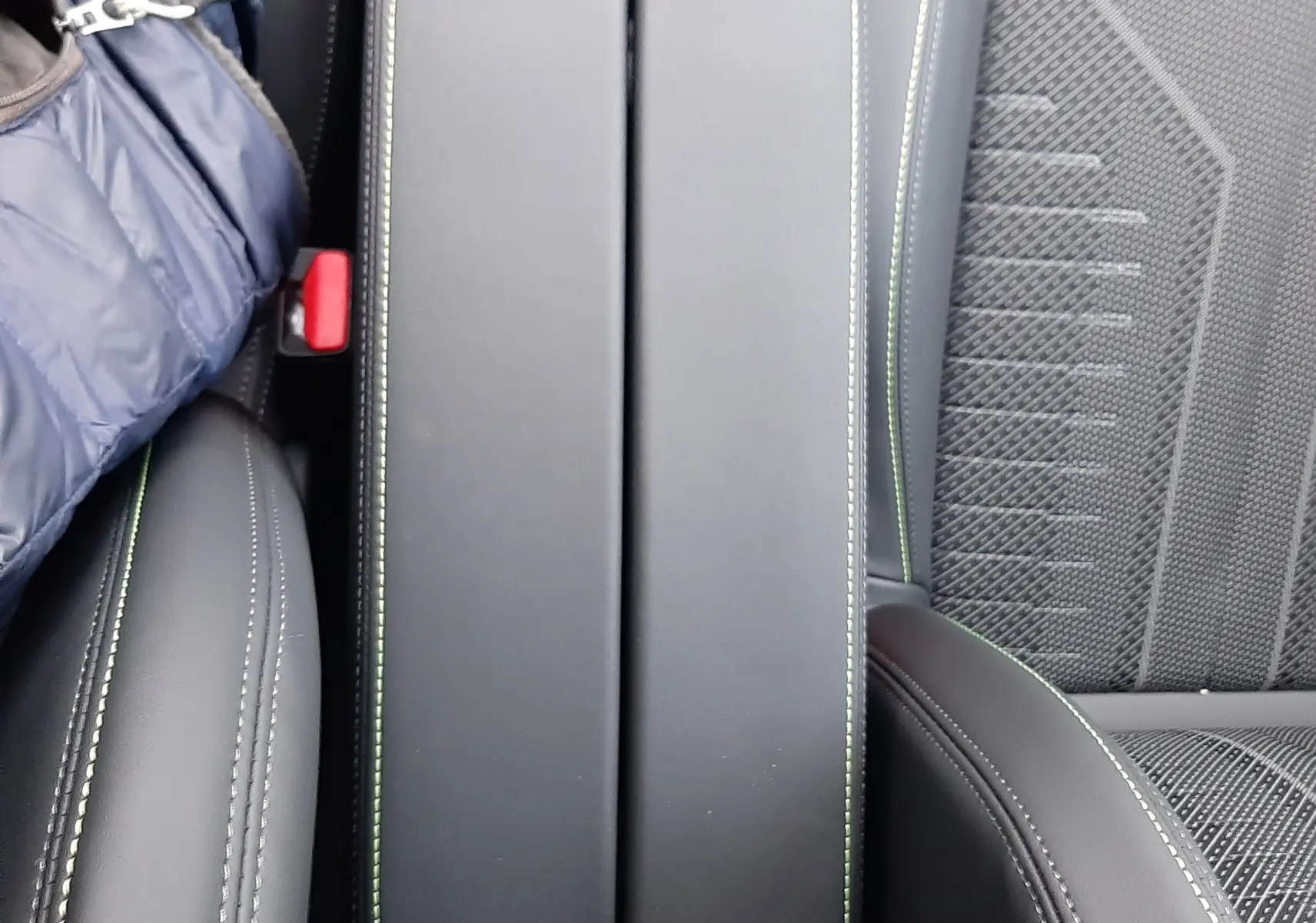 Vue rapprochée de l'accoudoir central noir avec surpiqûres vertes et sièges en tissu gris de la Peugeot 308 Hybrid 2025.