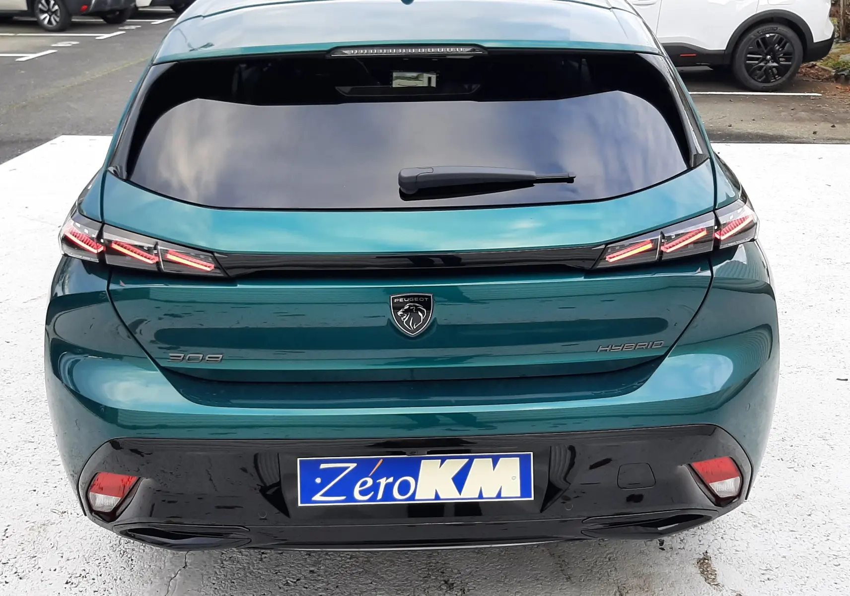Vue arrière d'une Peugeot 308 hybride bleu Lagoa avec feux LED distinctifs et plaque Zéro KM visible.