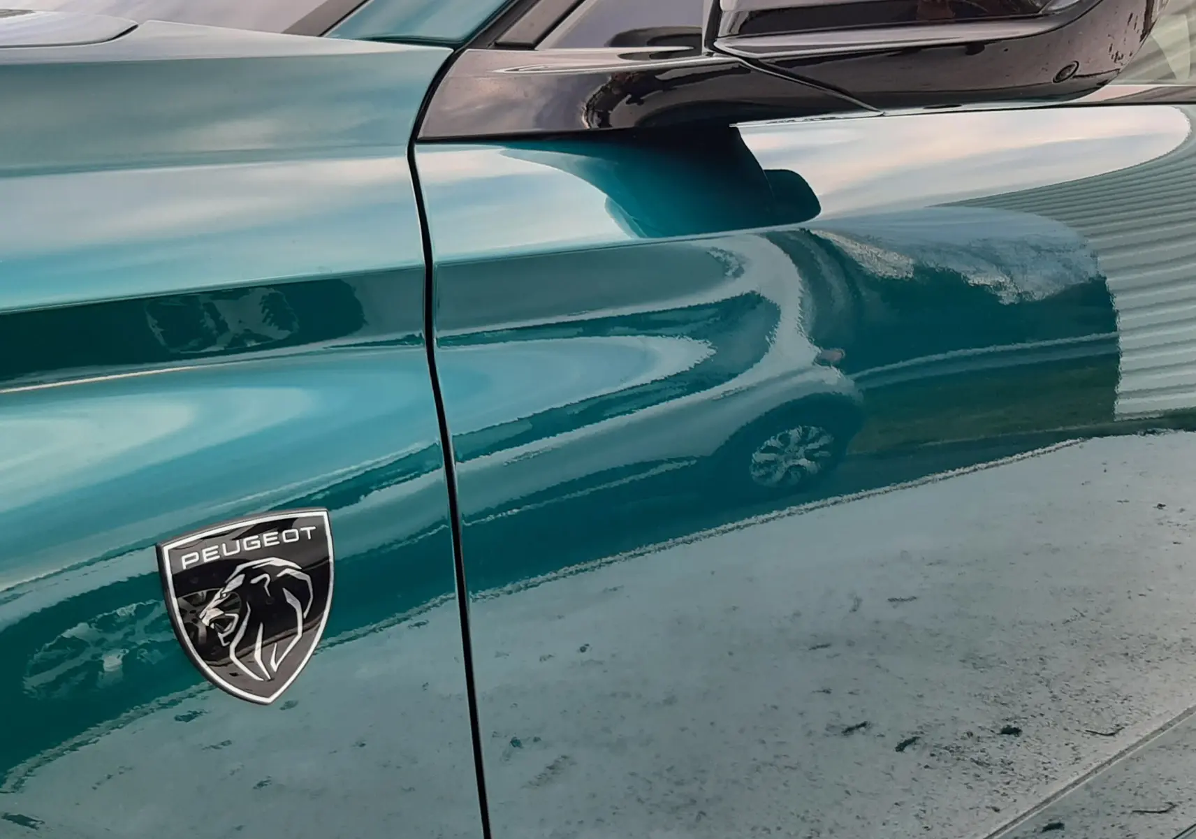 Gros plan sur la porte côté gauche d'une Peugeot 308 bleu Lagoa avec logo lion et rétroviseur noir brillant.
