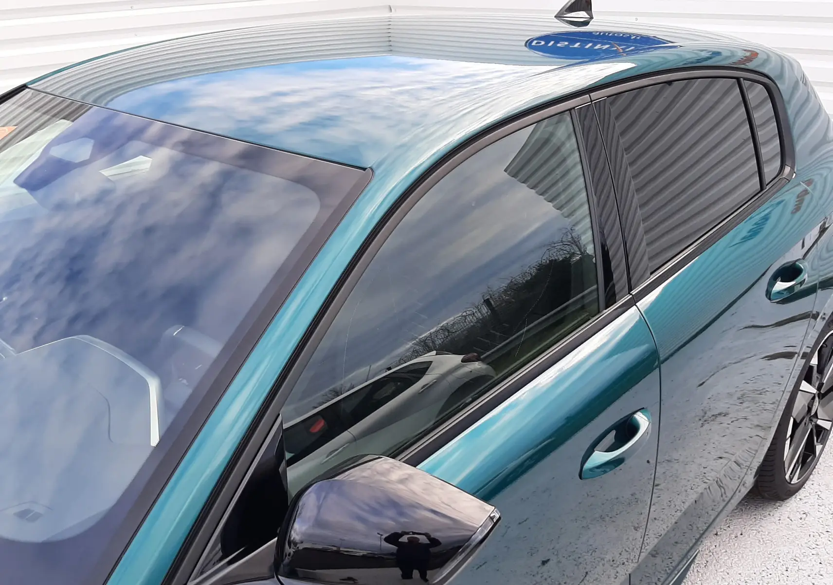 Vue de côté gauche avant d'une Peugeot 308 1.2 Hybrid 145ch GT en bleu Lagoa avec rétroviseur noir brillant.