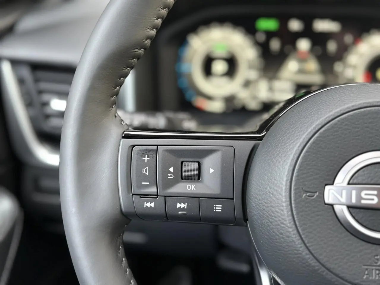 Gros plan sur le volant cuir gris du Nissan Qashqai 2025 avec commandes multifonctions et tableau de bord numérique flou en arrière-plan.