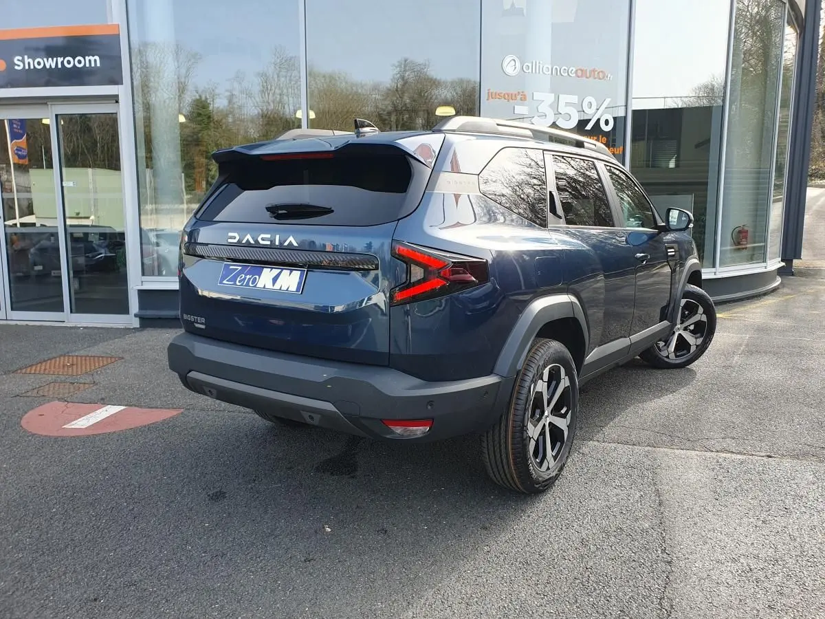 Vue 3/4 arrière droite d'un Dacia Bigster bleu indigo avec toit panoramique et jantes alliage diamantées.