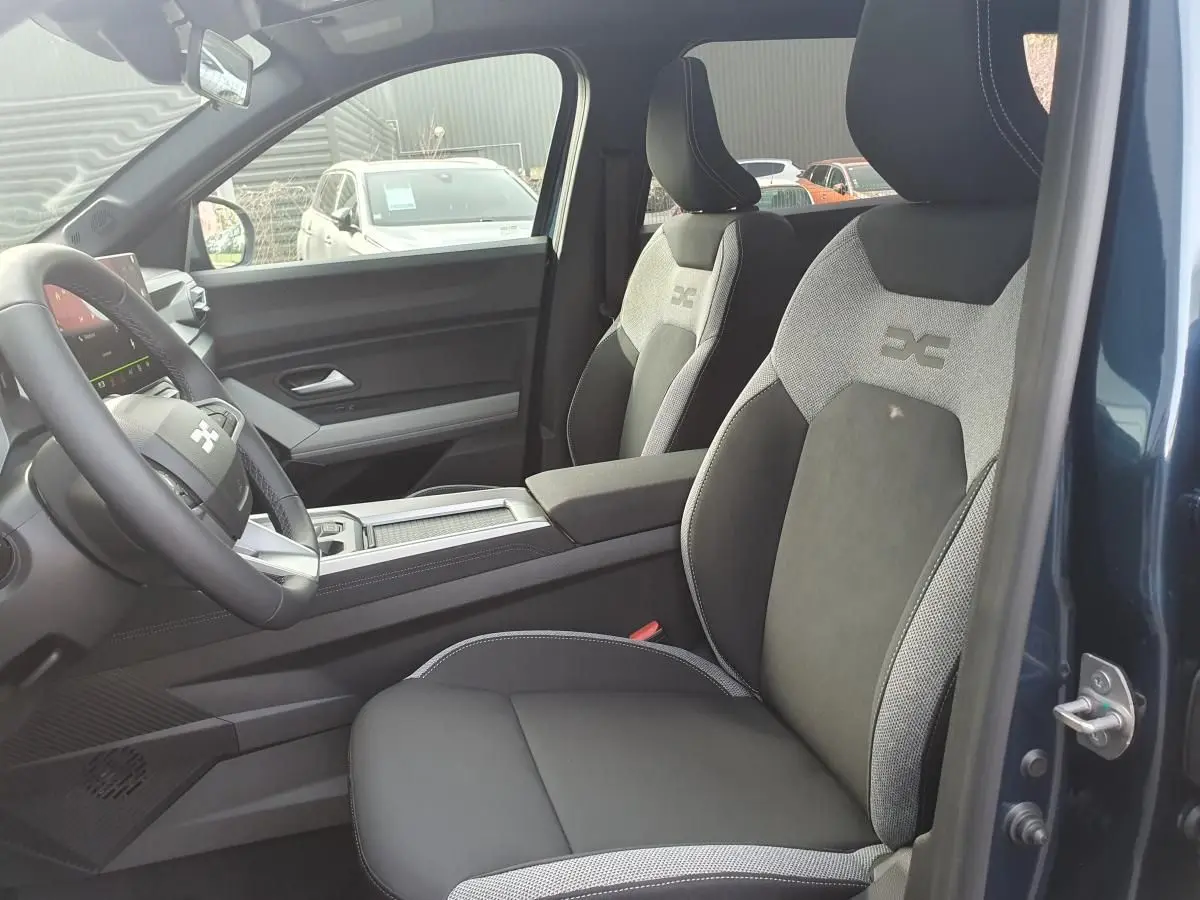 Vue intérieure côté conducteur du Dacia Bigster bleu indigo, mettant en valeur les sièges bi-matière avec logo brodé.